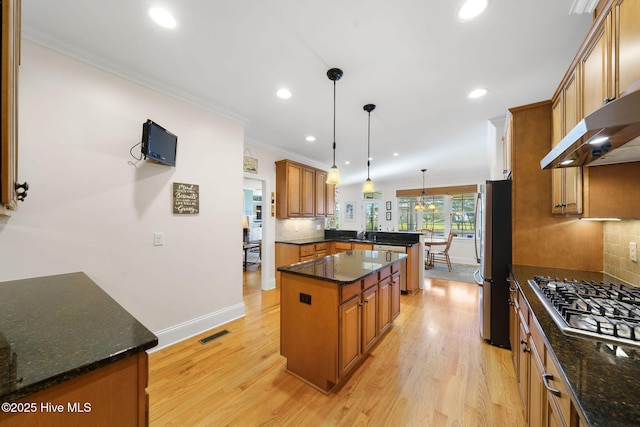 kitchen featuring a center island, stainless steel appliances, dark stone countertops, light hardwood / wood-style floors, and hanging light fixtures