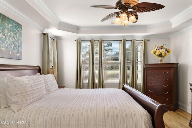 bedroom with ceiling fan, crown molding, light hardwood / wood-style floors, and a tray ceiling