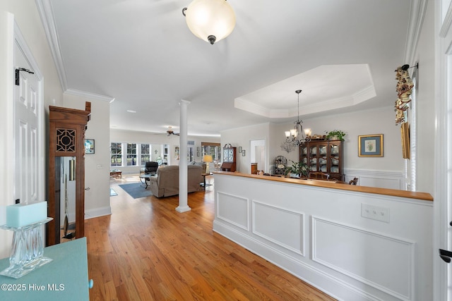 interior space featuring a notable chandelier, a raised ceiling, crown molding, light hardwood / wood-style flooring, and ornate columns