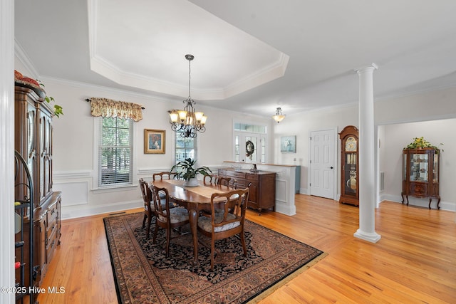 dining room with ornamental molding, a raised ceiling, ornate columns, and light wood-type flooring