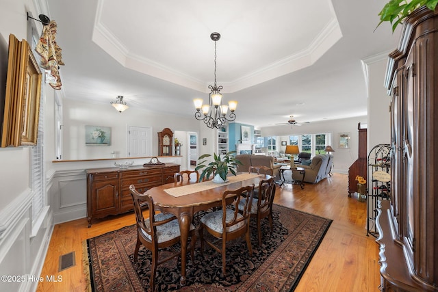 dining room featuring light hardwood / wood-style flooring, ceiling fan with notable chandelier, and a raised ceiling