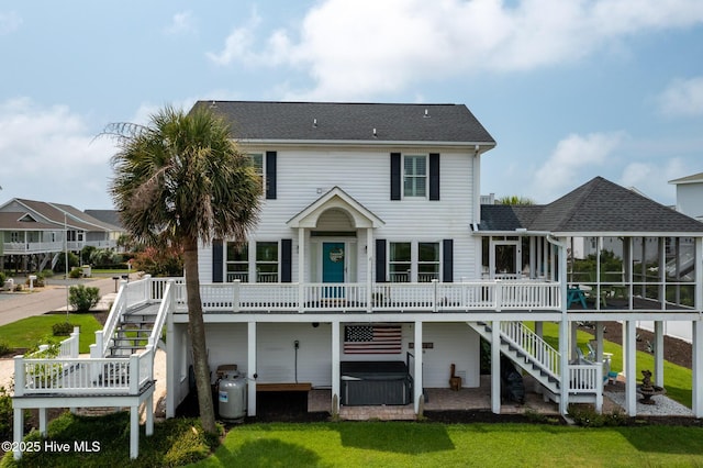 rear view of property featuring a wooden deck, a sunroom, a hot tub, and a yard