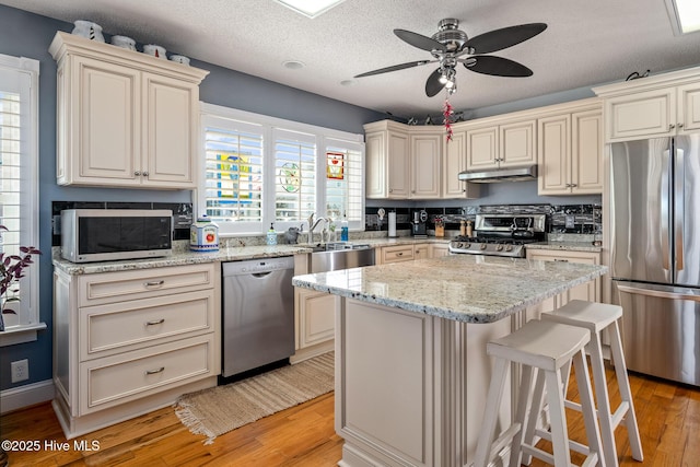 kitchen featuring cream cabinets, stainless steel appliances, light hardwood / wood-style flooring, a breakfast bar, and a center island