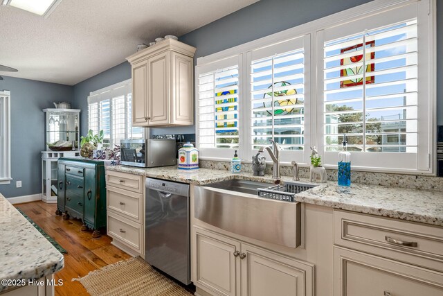 kitchen with appliances with stainless steel finishes, light wood-type flooring, a textured ceiling, light stone counters, and sink