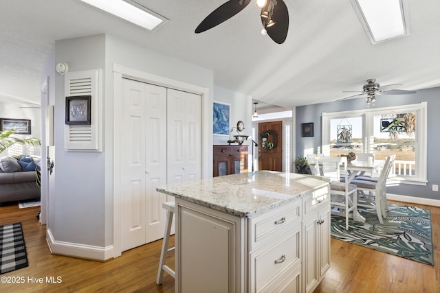 kitchen with a kitchen island, ceiling fan, light stone counters, a breakfast bar, and light hardwood / wood-style flooring