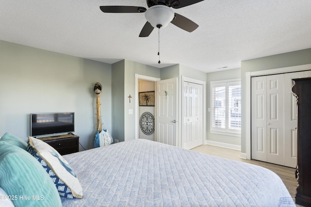 bedroom featuring ceiling fan, two closets, a textured ceiling, and light hardwood / wood-style flooring