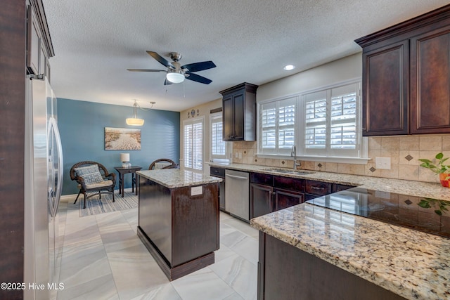 kitchen featuring sink, light stone counters, appliances with stainless steel finishes, a kitchen island, and pendant lighting