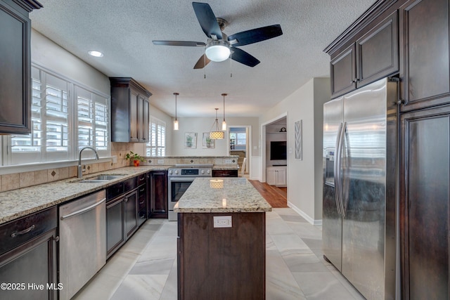 kitchen featuring sink, appliances with stainless steel finishes, hanging light fixtures, light stone countertops, and a kitchen island