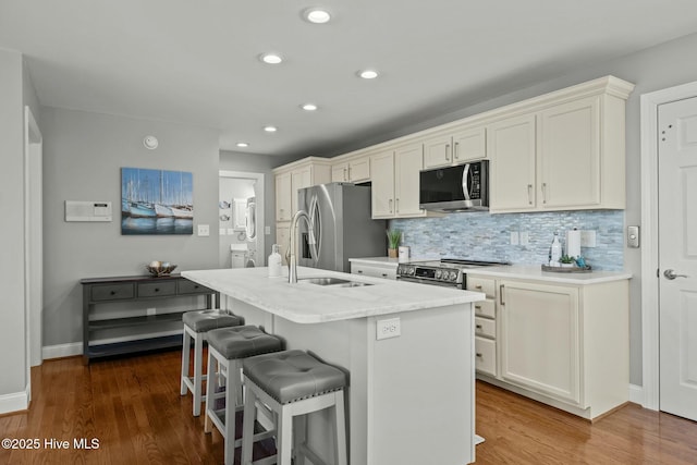 kitchen with tasteful backsplash, a kitchen island with sink, appliances with stainless steel finishes, a kitchen breakfast bar, and dark hardwood / wood-style flooring