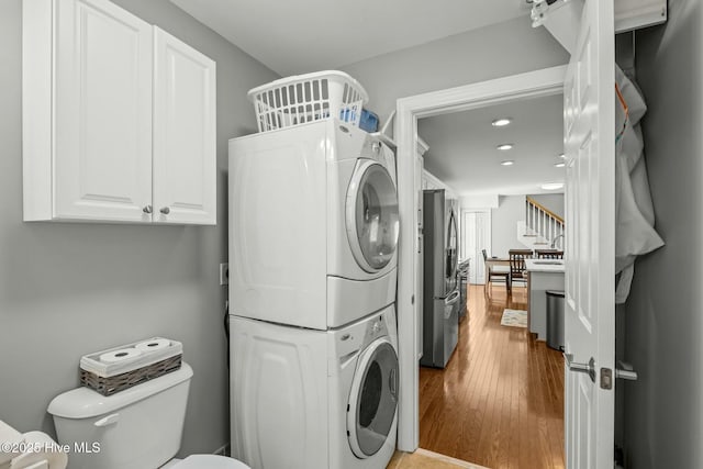 laundry room featuring stacked washer / dryer and light hardwood / wood-style flooring