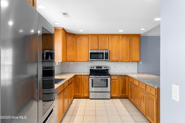 kitchen featuring tasteful backsplash, light stone countertops, stainless steel appliances, and light tile patterned flooring