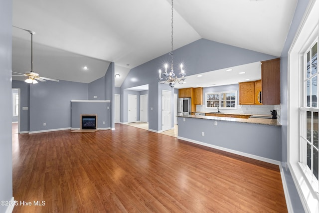 unfurnished living room with sink, ceiling fan with notable chandelier, high vaulted ceiling, and light wood-type flooring