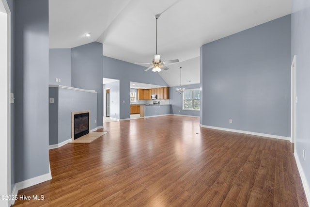 unfurnished living room with high vaulted ceiling, ceiling fan with notable chandelier, a fireplace, and light hardwood / wood-style flooring