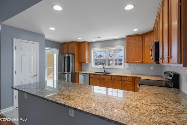 kitchen with sink, decorative backsplash, light stone counters, kitchen peninsula, and stainless steel appliances