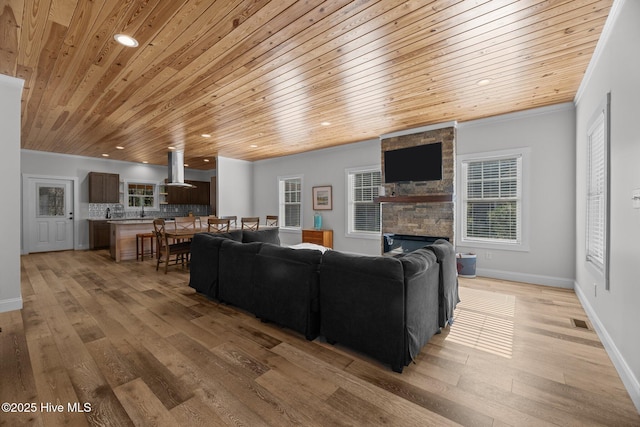 living room featuring crown molding, wooden ceiling, a fireplace, and light hardwood / wood-style flooring