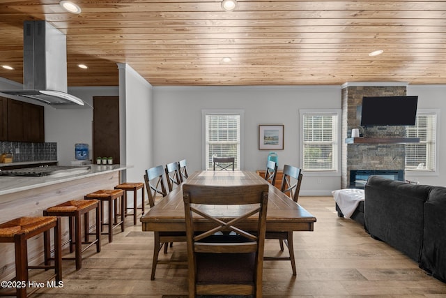 dining room featuring wood ceiling, a stone fireplace, and light wood-type flooring