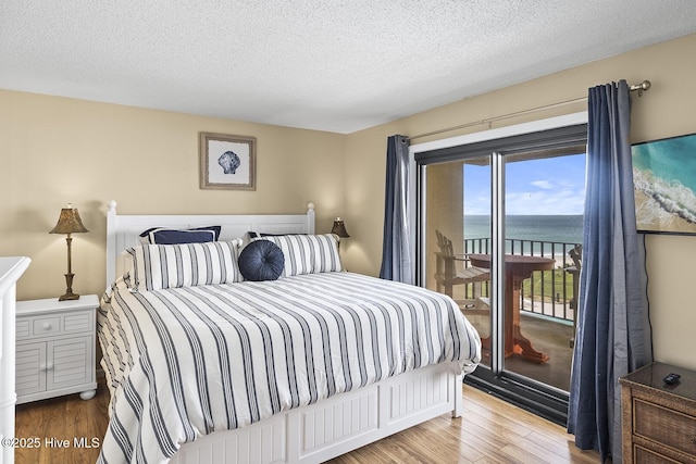 bedroom with access to outside, wood-type flooring, and a textured ceiling