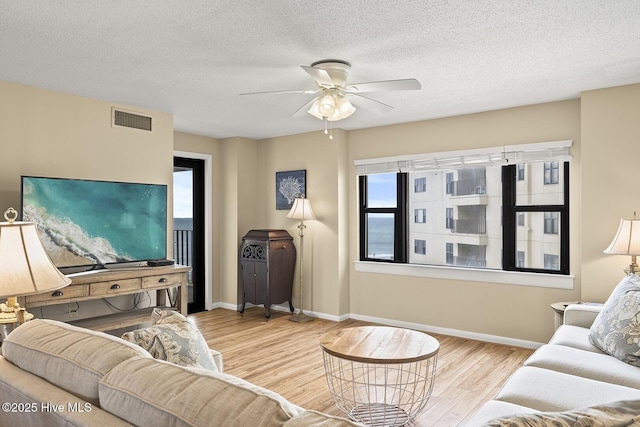 living room with ceiling fan, a textured ceiling, and light hardwood / wood-style flooring