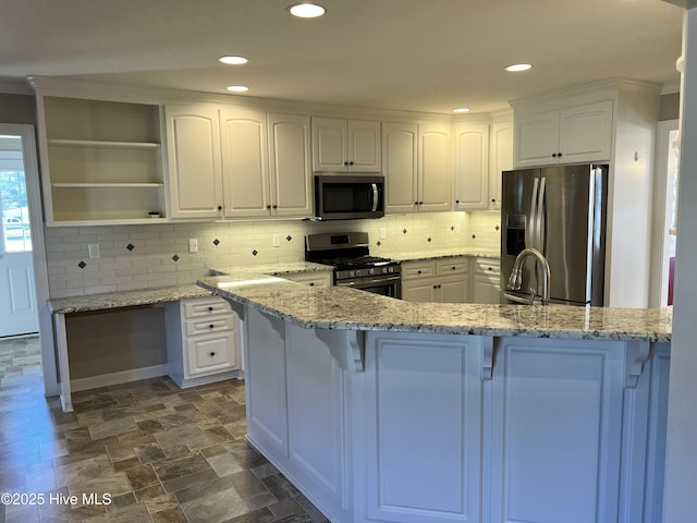 kitchen featuring kitchen peninsula, stainless steel appliances, white cabinets, and light stone counters