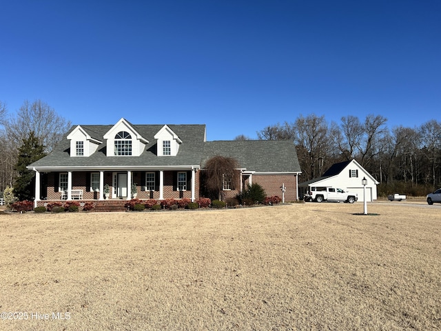 new england style home with covered porch, a front yard, and a garage