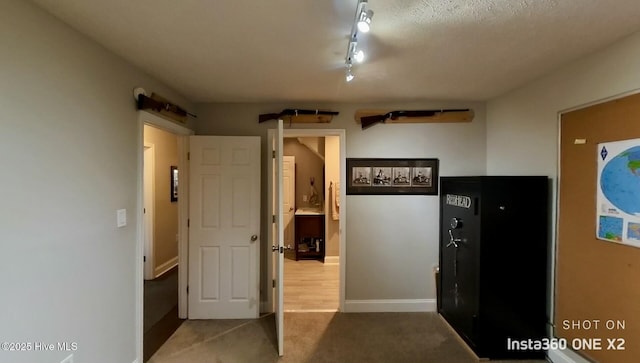 corridor featuring rail lighting, a textured ceiling, and carpet flooring