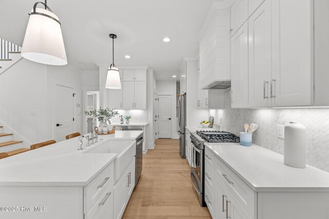 kitchen featuring a kitchen island with sink, a breakfast bar area, white cabinets, decorative light fixtures, and gas range