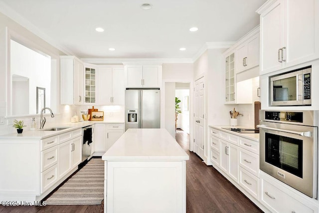 kitchen with white cabinetry, stainless steel appliances, backsplash, a kitchen island, and sink