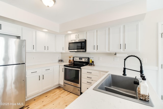 kitchen with sink, white cabinetry, appliances with stainless steel finishes, and light wood-type flooring