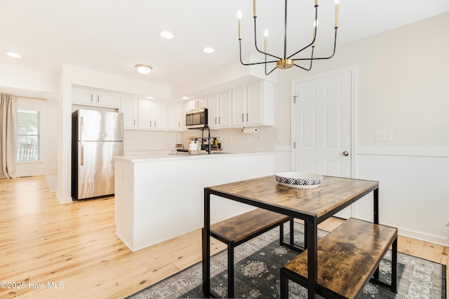 kitchen with light hardwood / wood-style floors, kitchen peninsula, white cabinets, and stainless steel appliances