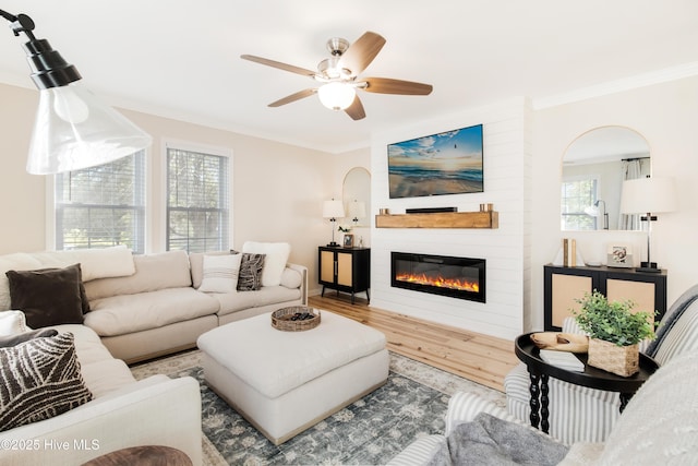 living room with ceiling fan, wood-type flooring, a large fireplace, and crown molding