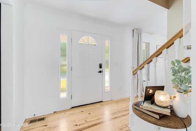 foyer entrance with a wealth of natural light, ornamental molding, and light hardwood / wood-style flooring