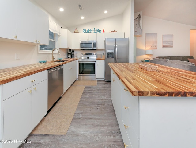 kitchen with sink, white cabinetry, lofted ceiling, butcher block countertops, and appliances with stainless steel finishes