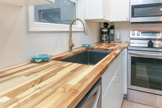 kitchen with appliances with stainless steel finishes, white cabinetry, butcher block counters, and sink