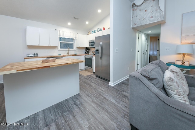 kitchen featuring stainless steel appliances, hardwood / wood-style floors, a kitchen island, butcher block countertops, and white cabinetry