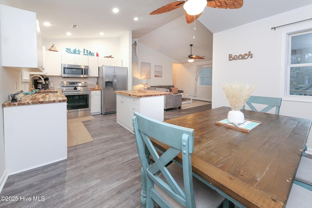 dining area with sink, hardwood / wood-style flooring, ceiling fan, and vaulted ceiling