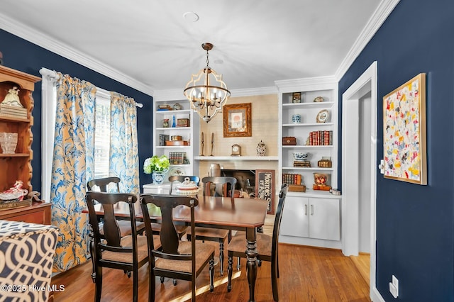 dining space with light wood-type flooring, built in features, a notable chandelier, and crown molding