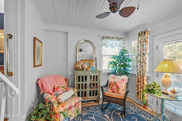 sitting room with ceiling fan, wooden ceiling, crown molding, and brick wall