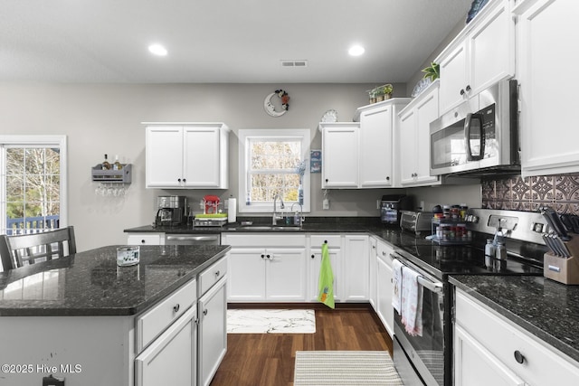 kitchen featuring a kitchen island, white cabinets, dark stone counters, appliances with stainless steel finishes, and sink