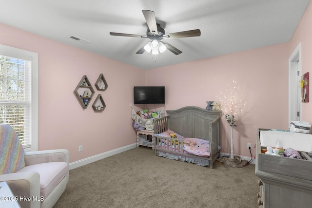 bedroom featuring a nursery area, ceiling fan, and carpet