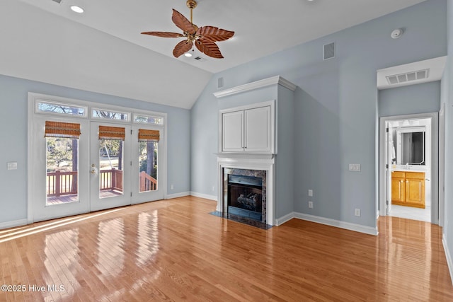 unfurnished living room with ceiling fan, vaulted ceiling, a premium fireplace, light hardwood / wood-style flooring, and french doors