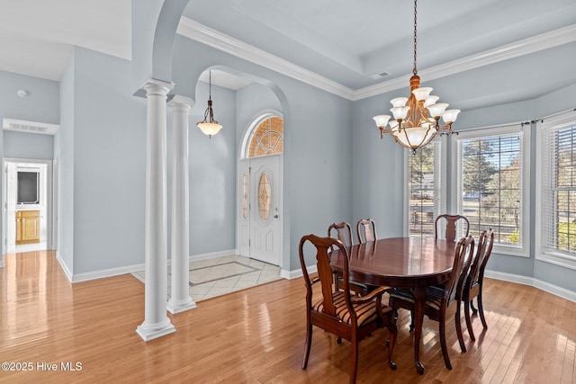 dining room with ornate columns, light hardwood / wood-style floors, a tray ceiling, and a notable chandelier