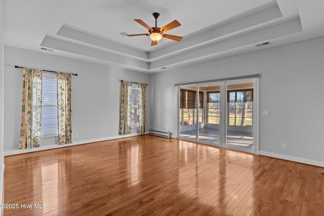 unfurnished room featuring a baseboard heating unit, a wealth of natural light, and a tray ceiling