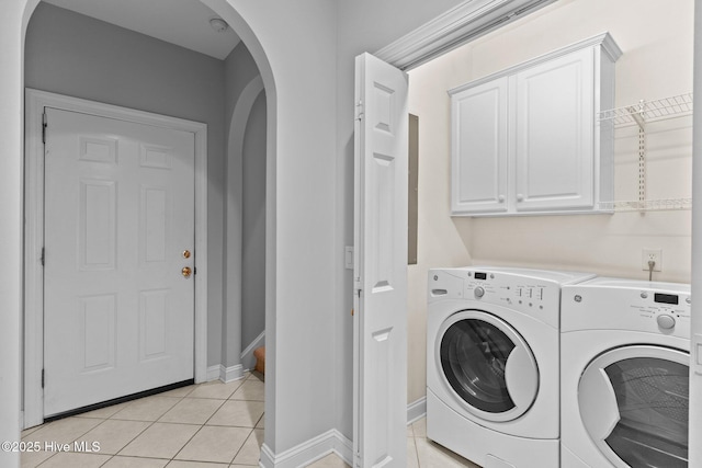 clothes washing area with washing machine and dryer, cabinets, and light tile patterned floors