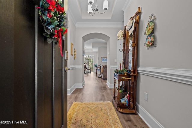 hallway featuring crown molding, hardwood / wood-style flooring, a tray ceiling, and a notable chandelier