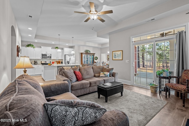 living room with ceiling fan, light hardwood / wood-style flooring, and a tray ceiling