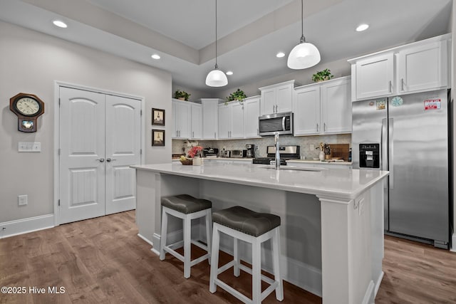 kitchen with white cabinetry, hardwood / wood-style floors, an island with sink, stainless steel appliances, and pendant lighting