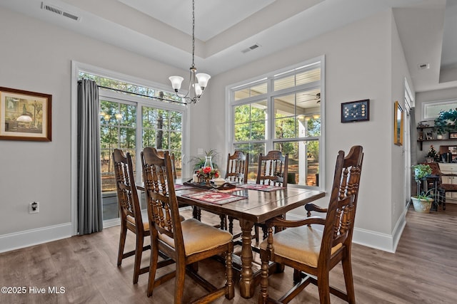 dining area with hardwood / wood-style flooring, a tray ceiling, and a notable chandelier