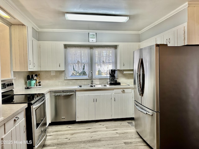 kitchen with sink, white cabinetry, light hardwood / wood-style flooring, ornamental molding, and appliances with stainless steel finishes