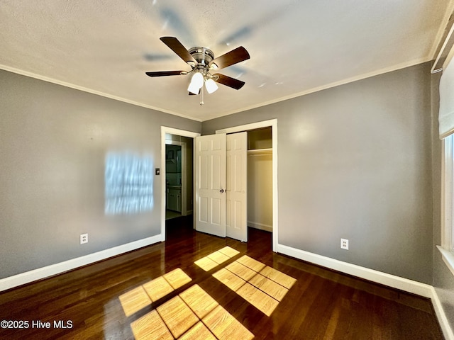 unfurnished bedroom featuring dark wood-type flooring, ceiling fan, crown molding, and a closet