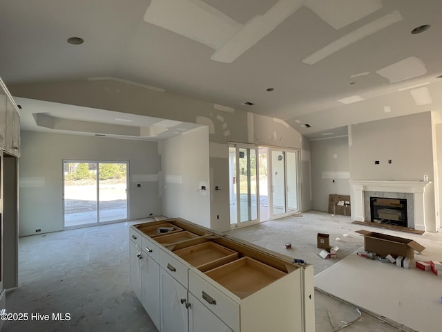 kitchen featuring a tile fireplace, white cabinetry, and lofted ceiling